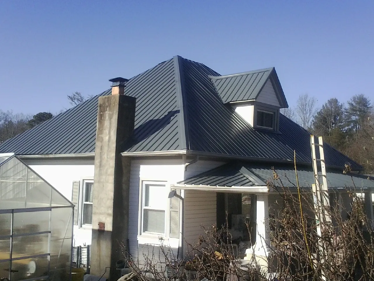 Dark blue standing seam metal roof on a white farmhouse with dormer — Slate & Tile Roof Repair by Roofing Brothers in Pen Argyl