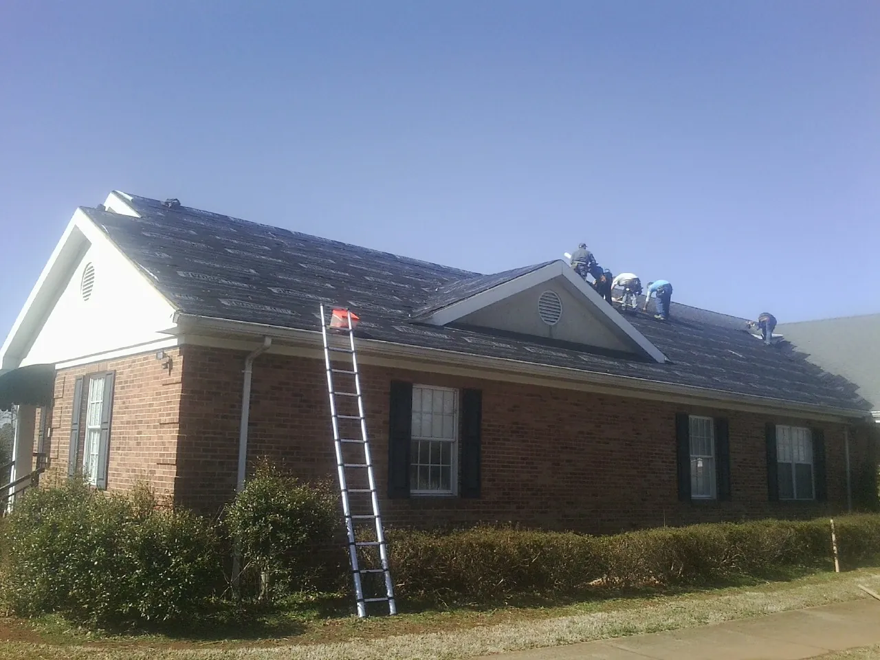 Crew tearing shingles off a brick ranch roof with a ladder set — Emergency Roof Repair work by our crew in Pen Argyl