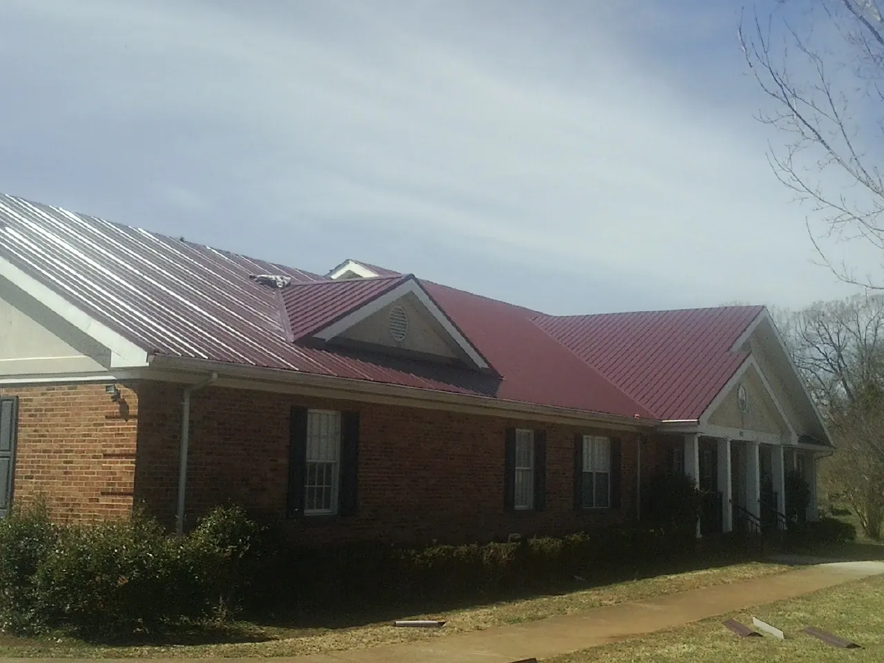 Red metal roof with gabled entries on a long brick building, from a Hail Damage Roof Repair job in Pen Argyl