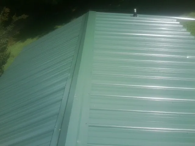 New green metal panels meeting at the ridge of a roof — Flat Roof Repair work by our crew in Pen Argyl