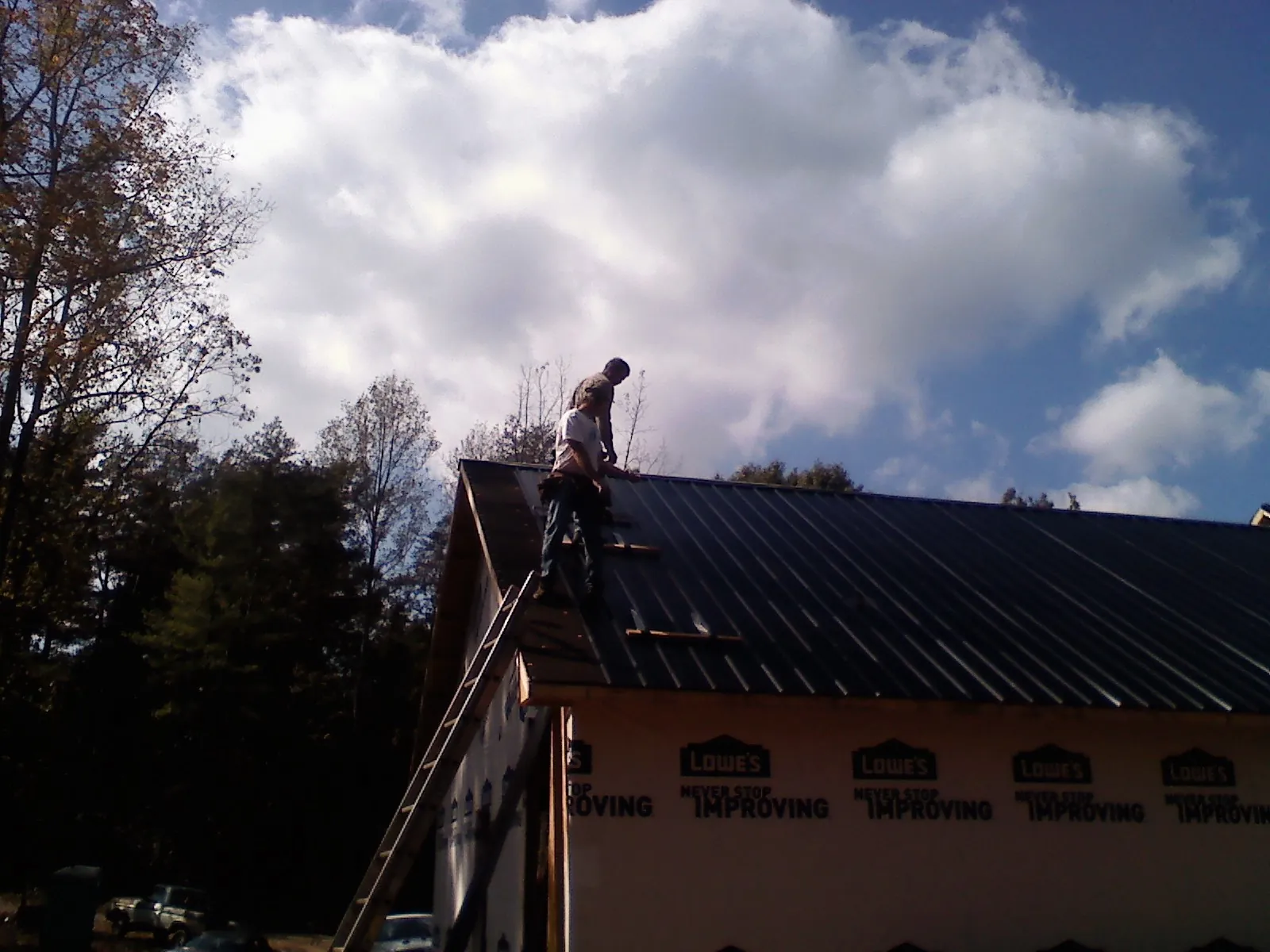 Roofer fastening dark metal panels high against a cloudy sky, from a Roof Inspection job in Pen Argyl