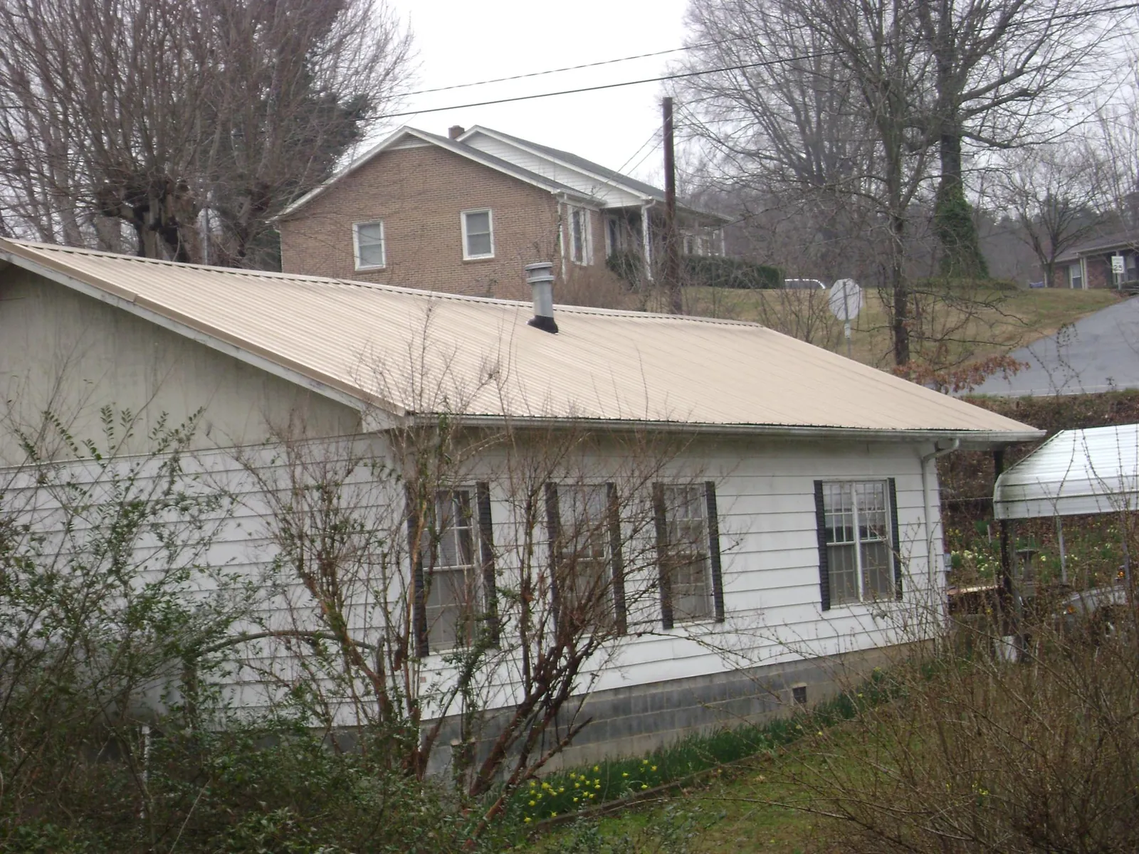 Tan metal roof on a white sided house set into a hillside — Commercial Roofing by Roofing Brothers in Pen Argyl
